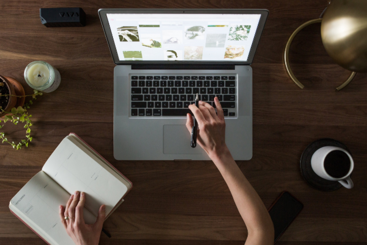 A person working on a laptop with a notebook, coffee, and plants, symbolizing productivity and motivation in challenging economic times.