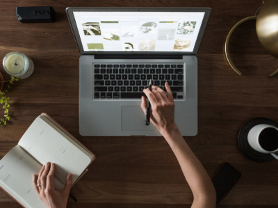 A person working on a laptop with a notebook, coffee, and plants, symbolizing productivity and motivation in challenging economic times.