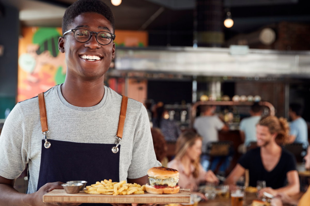 Smiling restaurant server holding a burger and fries, showcasing restaurant dining experience and financing opportunities.