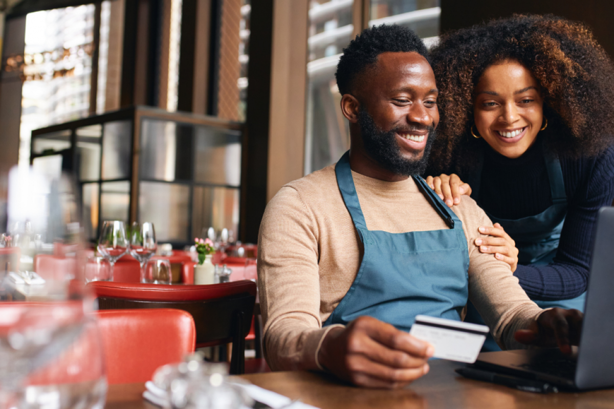 Restaurant owners exploring financing options while using a laptop and credit card in a vibrant dining setting.